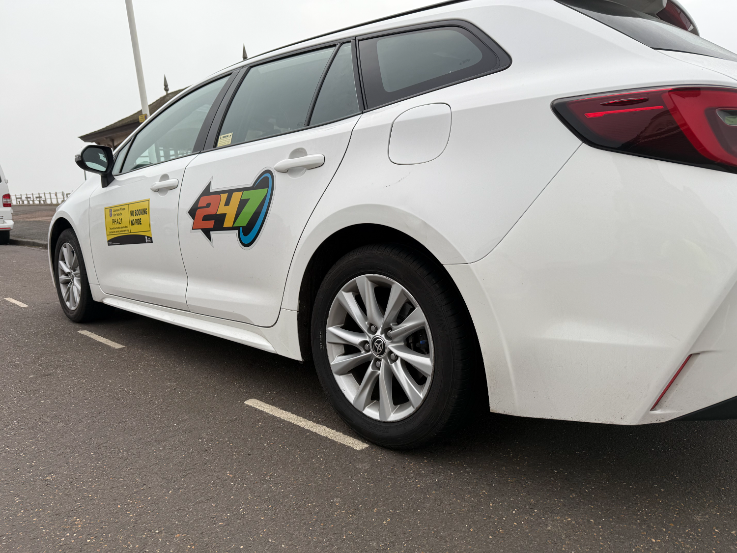 A white 247 Taxis Toyota Corolla parked on Hastings seafront